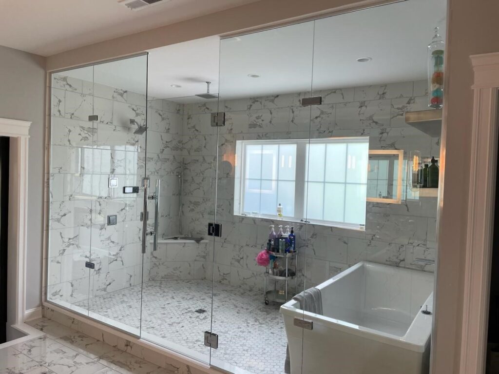 A large frameless shower  door enclosing a shower, steam room, and bathtub with a window.